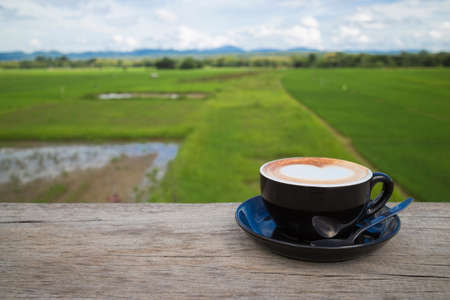 Black coffee cup with cappuccino on wooden table with Blue Sky and green Paddy Beautiful natural morning background, image with copy space.の写真素材
