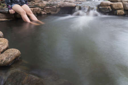 The girl soaked her legs in a Waterfall hot spring in Lampang Thailand and Relaxing in a natural hot bath.の写真素材