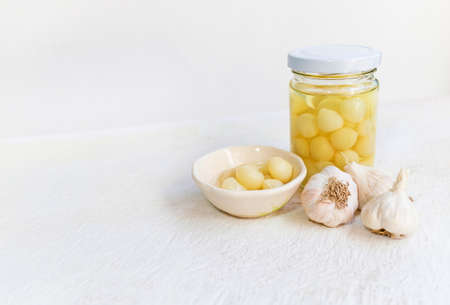 Pickled garlic in a glass jar and Pickled garlic in a bowl with garlic on a white wooden table and white background, image with copy space for text or image.の写真素材