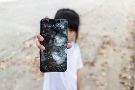 Child girl holding a Broken Smartphone and broken touch screen on hand, image with copy space.の写真素材