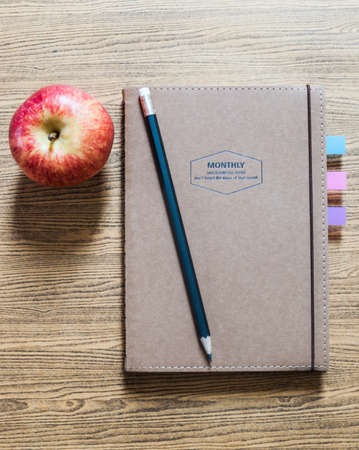 recycled paper notebook with a pencil and an apple on wooden backgroundの写真素材