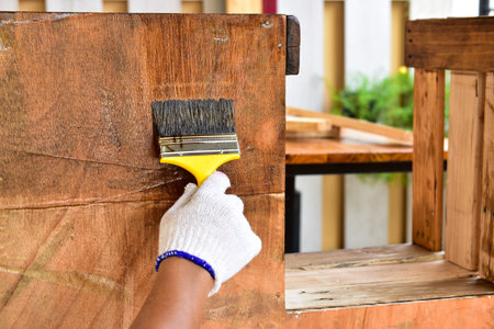 The painter uses the lacquer paint to the wooden furniture with a yellow brush. He worked with...