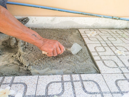 The worker's hand is putting tiles adhesive to the floor with the notched trowel
