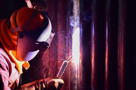 The welder is welding the pipe wall with Shielded metal arc welding process (SMAW). The welder wears protective equipment with a mask and heat resistant gloves.の写真素材
