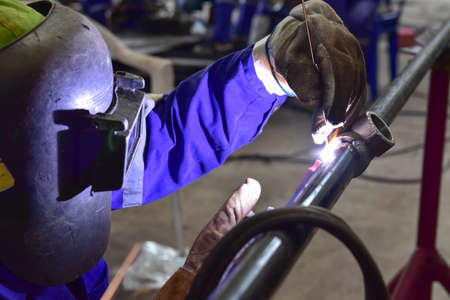 The welder is welding the pipeline with Tungsten Inert Gas Welding process (TIG). The welder wears protective equipment with a mask and heat resistant glovesの写真素材