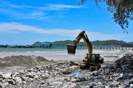 Crawler excavator are moving rocks to make breakwater on the beach. The beach , mountains and blue...