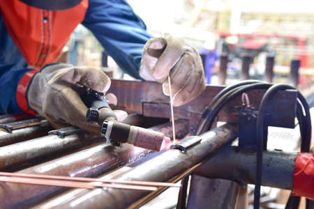 The welder is welding the plate to the pipe with Tungsten Inert Gas Welding process (TIG). The welder wears protective equipment with a mask and heat resistant glovesの写真素材