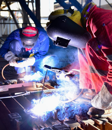 Two welder is assembling the workpiece by process shielded metal arc welding (SMAW). Welder in red...