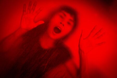 No panic,woman screaming behind stained or dirty window glass,Scary background for book coverの写真素材