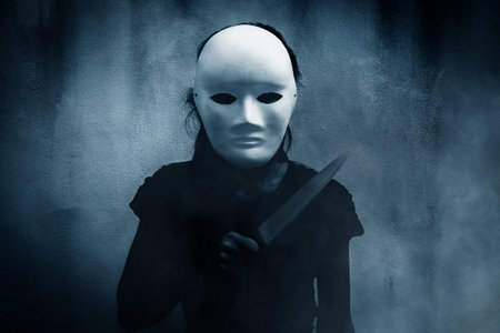 Mysterious woman in black wearing white mask with knife,Scary background for book coverの写真素材