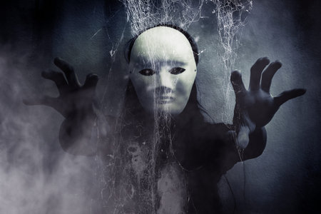 Mysterious woman in black wearing white mask hidden behind spider web,Scary background for book coverの写真素材