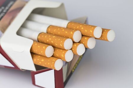 Cigarettes packed in red paper envelopes The cigarette end or cigarette end is brown and the tip is white and the end of the cigarette or cigarette end extends beyond the package on the white surface.の写真素材