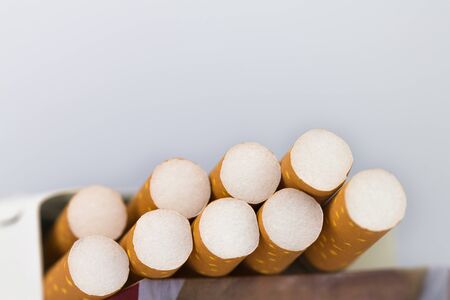 Cigarettes packed in red paper envelopes The cigarette end or cigarette end is brown and the tip is white and the end of the cigarette or cigarette end extends beyond the package on the white surface.の写真素材