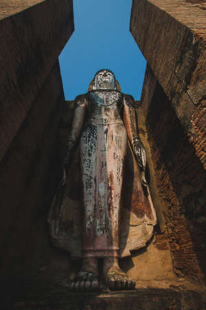 The large old Buddha statue Enshrined stands majestically in the Sukhothai Historical Park. Amid the orange-coloured sky during the evening, Sukhothai Province, Thailandの写真素材