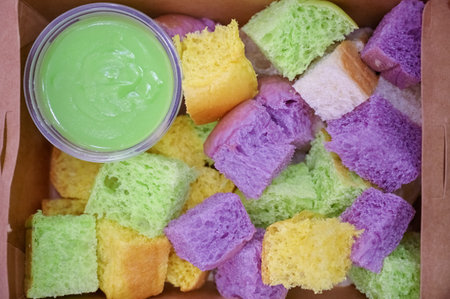 Sliced steamed multi-colored bread served in a go box with pandan custard dip