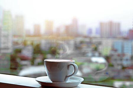 hot drink coffee cup near glass window  and city  blur backgroundの写真素材