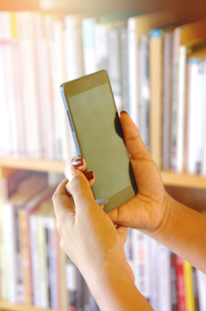 smartphone on women hand and  blur show book backgroundの写真素材