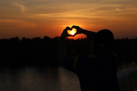 A young woman with a heart shaped hand During sunsetの写真素材