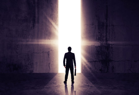 Businessman looking out of abstract opening in wall with bright daylight in concrete interior....