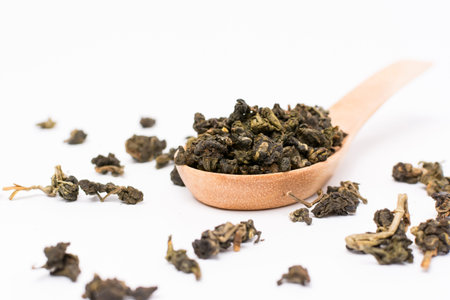 Green tea leaves in wooden scoop on white