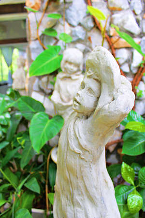 A statue of a stone carving of a girl wearing a hat and a tree around.の写真素材