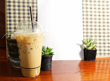 Cold coffee in clear plastic glass on wooden table, cactus background, white paper background and brown pattern.の写真素材