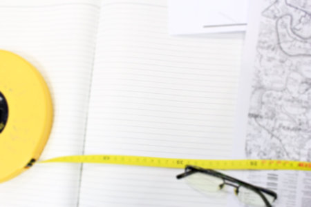 White Note on the desk with long yellow measuring tape. Eye glasses with maps