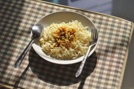 Instant noodles, noodles and sauces in a spoon and practice on the table top Brown fabric pattern with warm morning sunlightのeditorial素材