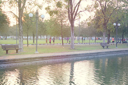 Morning light in the park with jogging people. There is a bench on the water.のeditorial素材