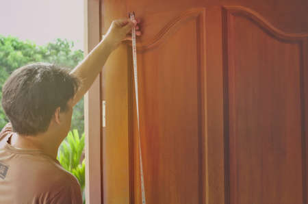 Working door repairman, measuring length with meter cable Of brown wood doors With the morning sunのeditorial素材