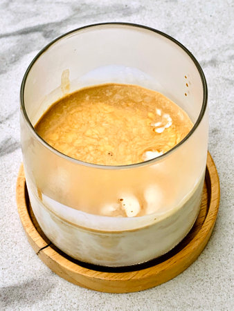 Dirty coffee menu, specialty coffee, is combination between the 'cold milk' at the bottom of the cup and the 'shot espresso' or 'ristretto' on top, placed on wooden saucer and marble table background.の写真素材