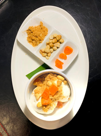 Fresh coconut milk ice cream topped with roasted pork floss, peanuts, salted egg in white plate on dark background.の写真素材