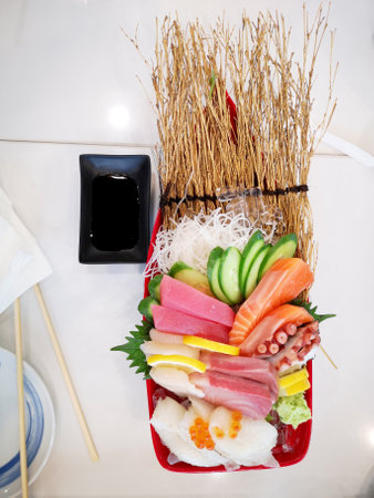 Sashimi is a Japanese delicacy that consists of fresh raw fish cut into thin slices, octopus tentacles, shrimp eggs, garnished with vegetables such as sliced lime, sliced radishes, sliced cucumber,  seasoned with soy sauce, and wasabi, eaten by bamboo chopsticks on white background.の写真素材