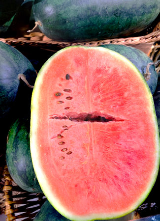 Vertical close-up view of whole and one red cut watermelons pitted in the wooden baskets. The concept for copy space or texture background.の写真素材