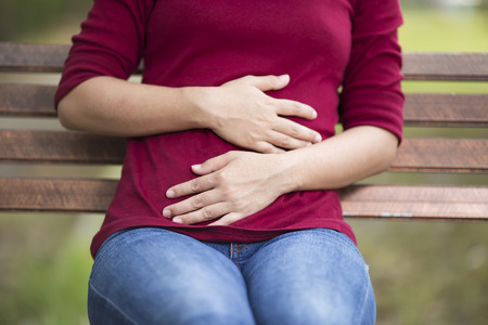 Woman Has Stomach Ache Sitting on Bench at Parkの写真素材