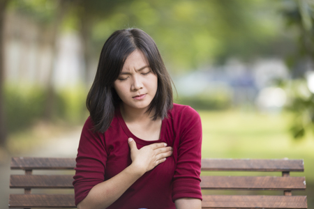 Woman Has Chest Pain Sitting on Bench at Parkの写真素材