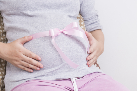 Pregnant woman tie a pink ribbon on her bellyの写真素材