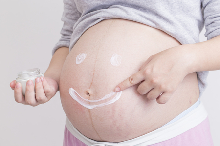 Pregnant woman applying skin care cream on bellyの写真素材