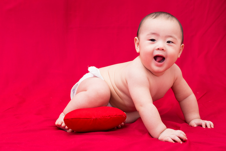 Asian baby with heart pillow on red backgroundの写真素材