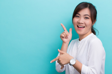 Asian woman pointing to the copy space isolated on blue backgroundの写真素材