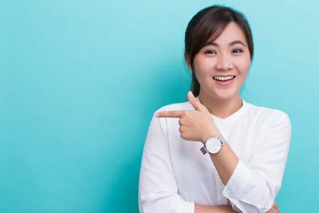 Asian woman pointing to the copy space isolated on blue backgroundの写真素材