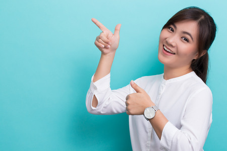 Asian woman pointing to the copy space isolated on blue backgroundの写真素材