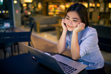 Shy woman using laptop in night time at cafeの写真素材
