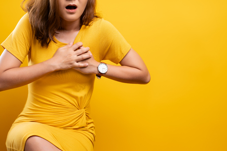 Woman has chest pain isolated over yellow backgroundの写真素材