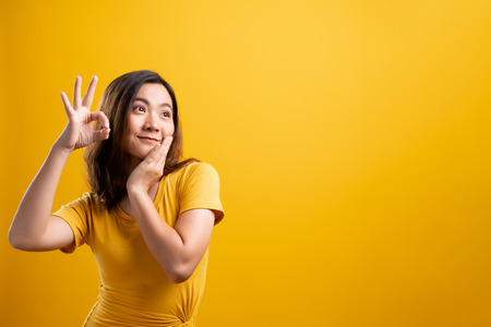 Happy woman showing OK gesture isolated on yellow backgroundの写真素材