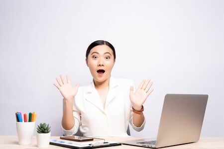 Portrait of a excited woman sitting at office isolated over backgroundの写真素材