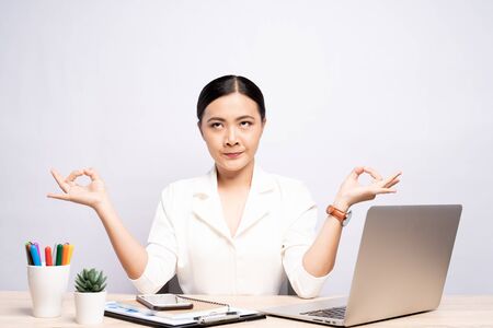 Woman meditating holding her hands in yoga gesture at office isolated over backgroundの写真素材