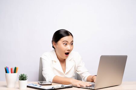 Portrait of a excited woman sitting at office isolated over backgroundの写真素材