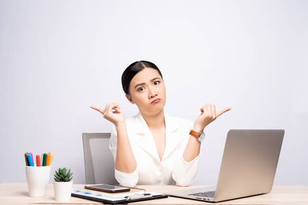 Portrait of a confused woman sitting at office isolated over backgroundの写真素材