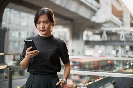 Happy asian woman looking at her phone in the cityの写真素材
